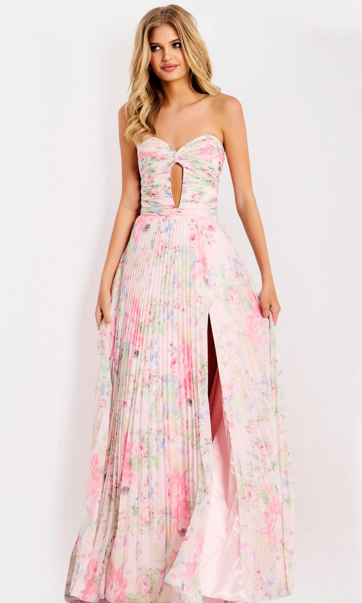 A woman in the Jovani 44518 long prom dress—strapless, floral, with a front cutout and thigh-high slit—stands against a white background. This pink chiffon gown is elegant and modern, ideal for any special occasion.